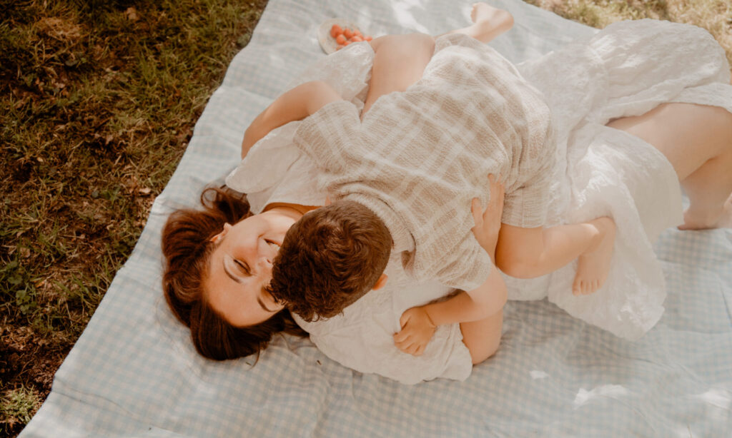 Moeder en zoon lachend liggend op een kleedje tijdens een motherhoodshoot