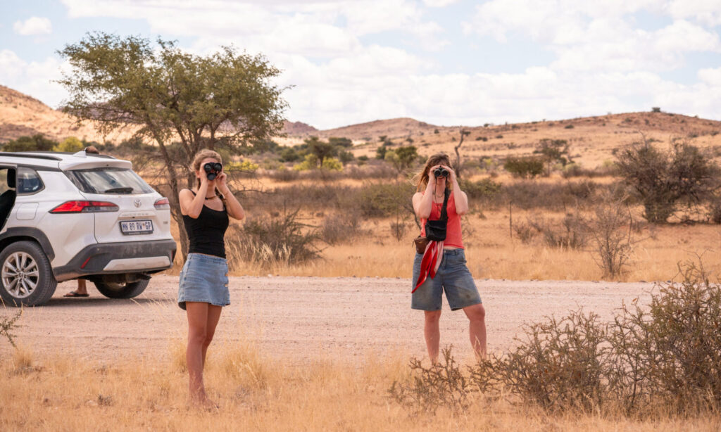 Foto van twee vriendinnen beiden met een verrekijker tijdens een shoot in het buitenland